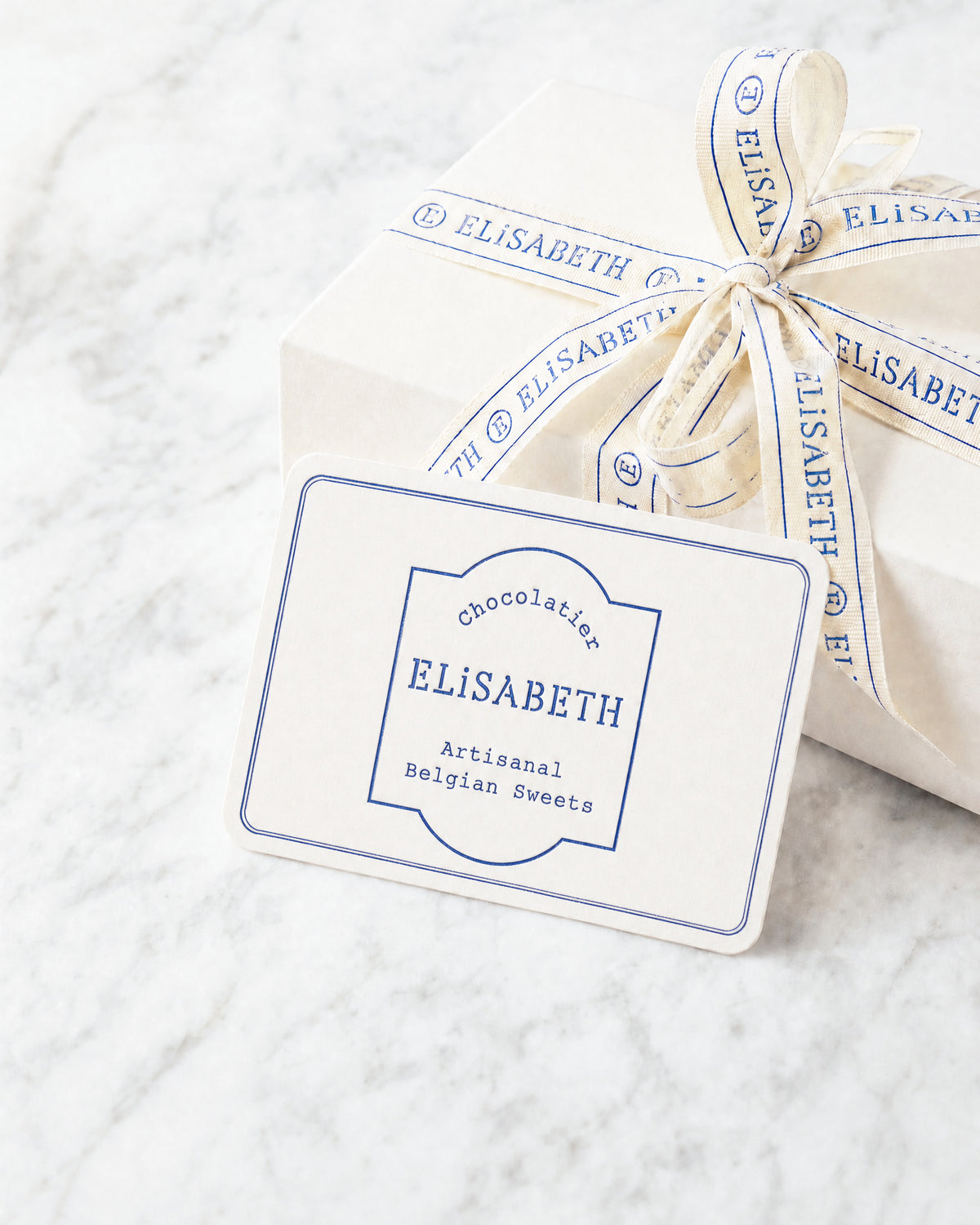 Cadeaubon van Elisabeth, ivoorkleurige kaart met blauw ecusson naast een geschenkdoos met lint